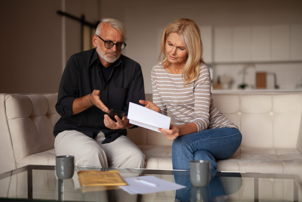 A couple in their late 50s or early 60s look concerned as they read financial paperwork © Adobe Stock