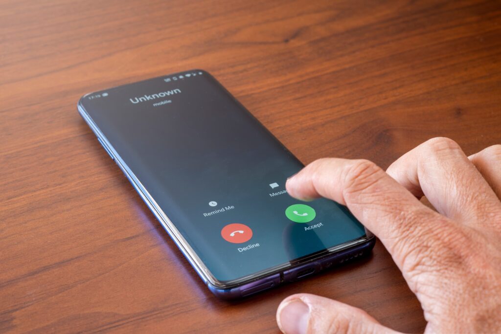 A smartphone has an incoming call from an unknown. The phone user's right hand is poised over the accept or decline call buttons.
