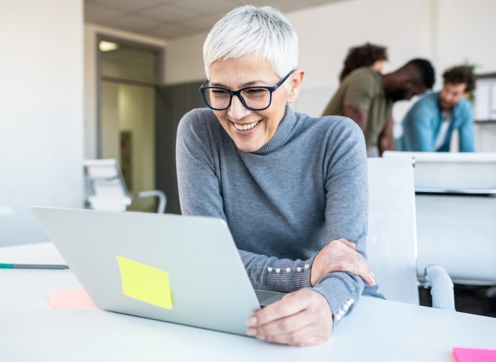 A smart, middle-aged lady smiles as she looks at her open laptop. A smart, middle-aged lady smiles as she looks at her open laptop.