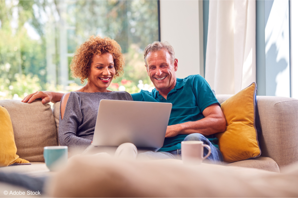 GBPensions April 1st tax changes-Image © Adobe Stock-Middle age couple with laptop 150dpi A middle-age couple are sitting on a couch with mugs of coffee smiling at their open laptop